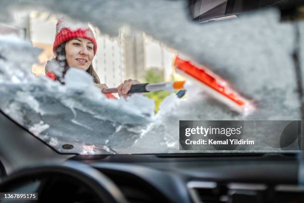 millennial woman in winter jacket scraping ice and snow from car windows - orange glove stock pictures, royalty-free photos & images