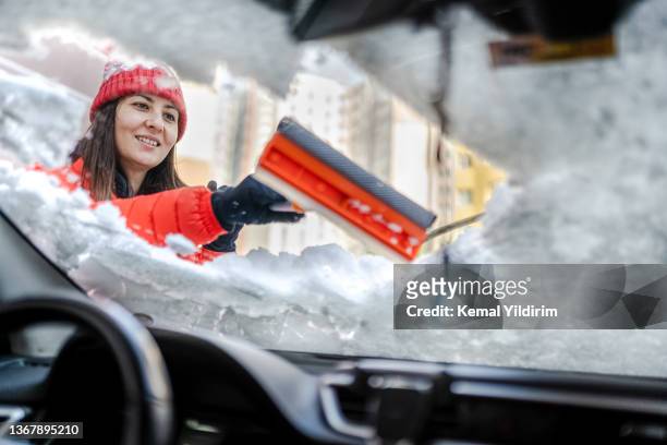 millennial-frau in winterjacke kratzt eis und schnee aus autofenstern - scraping stock-fotos und bilder