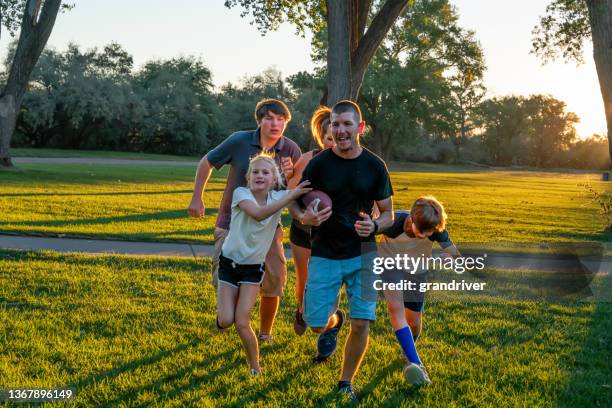 young family of five enjoying touch football together in the early evening at a park in the late summer stock photo - american football family stock pictures, royalty-free photos & images