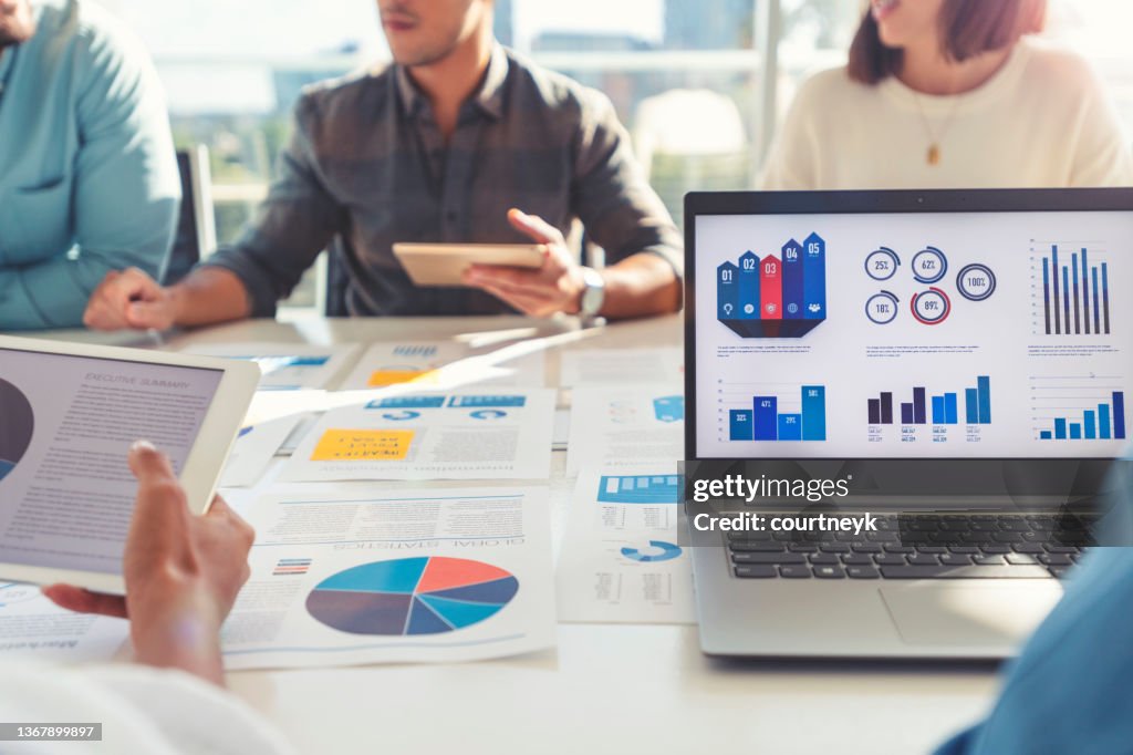 Group of people meeting with technology and paperwork.