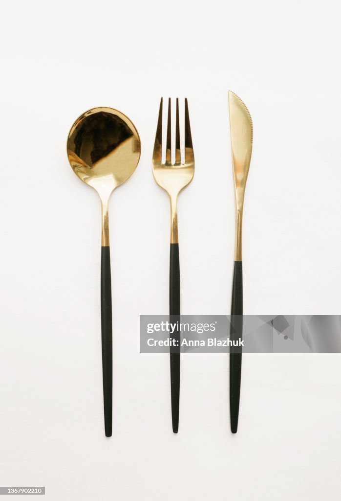 Black and golden fork, knife and spoon over white background