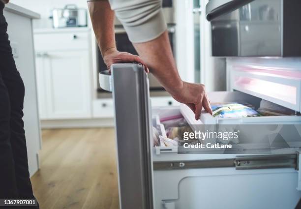 nicht identifizierbarer mann, der in eine geöffnete gefrierschublade eines kühlschranks schaut - gefrierkost stock-fotos und bilder
