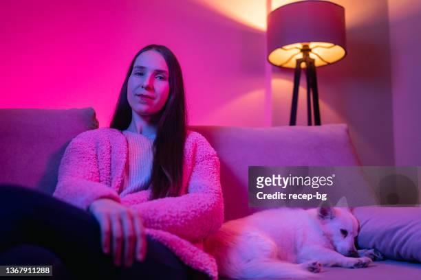 woman sitting next to her dog sleeping next to her at home - warm roze stockfoto's en -beelden