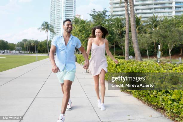 a multiracial millennial man with a beard and a caucasian millennial woman with long dark hair, happily walk together in an outdoor park, wearing casual summer clothing. - miami people stock pictures, royalty-free photos & images