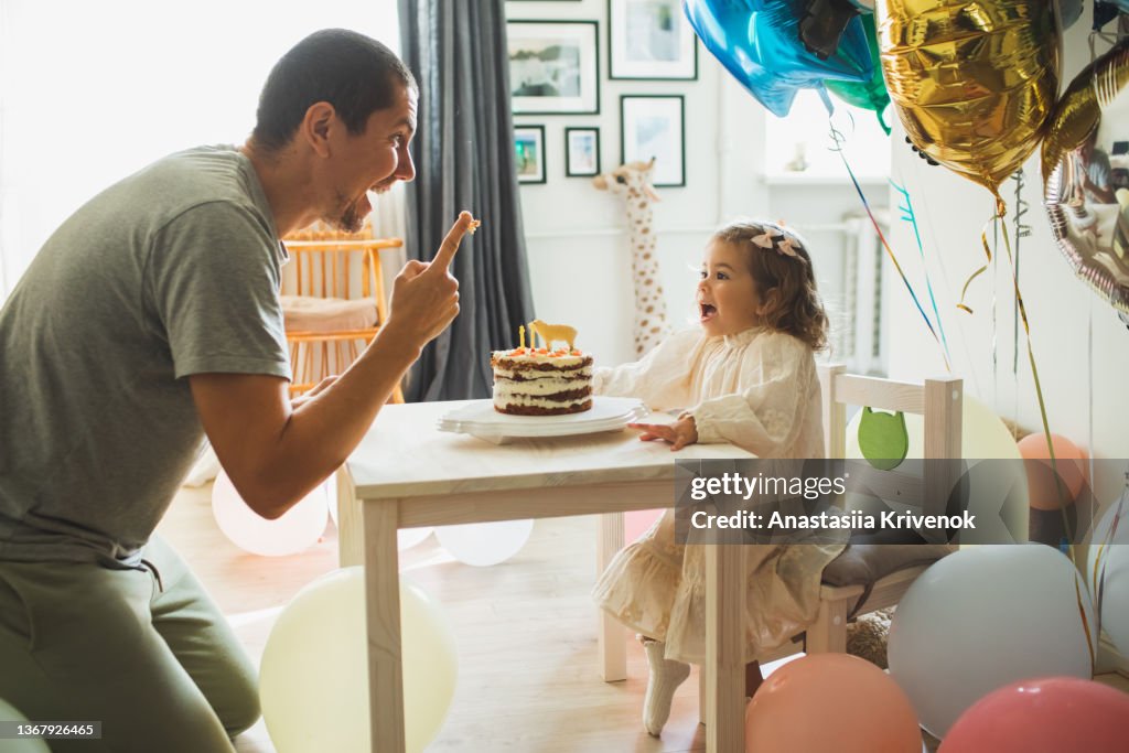 Young girl with father eating cake and having fun for celebreating her 2th years birthday.
