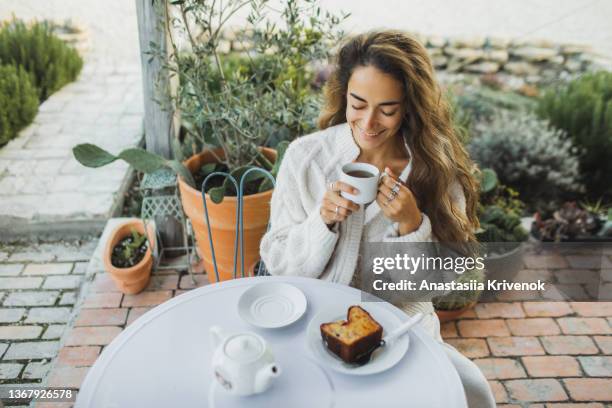 woman in a knitted white sweater drinking tea on cozy terrace of her house. - té terraza fotografías e imágenes de stock