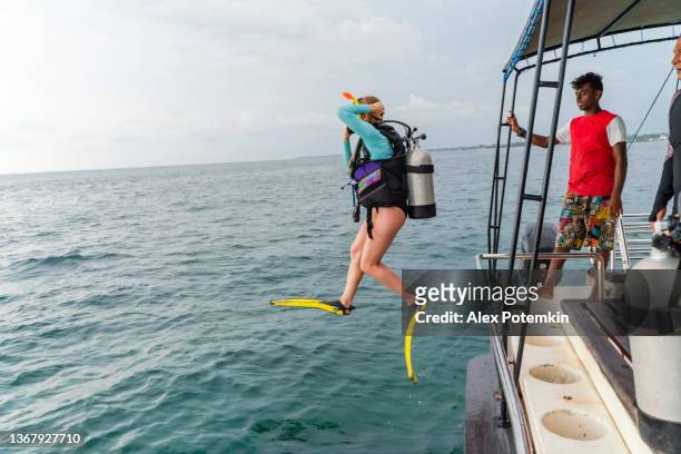 una mujer - buceador con un traje de buceo y aqualung, está saltando al océano desde un barco. - aqualung diving equipment fotografías e imágenes de stock