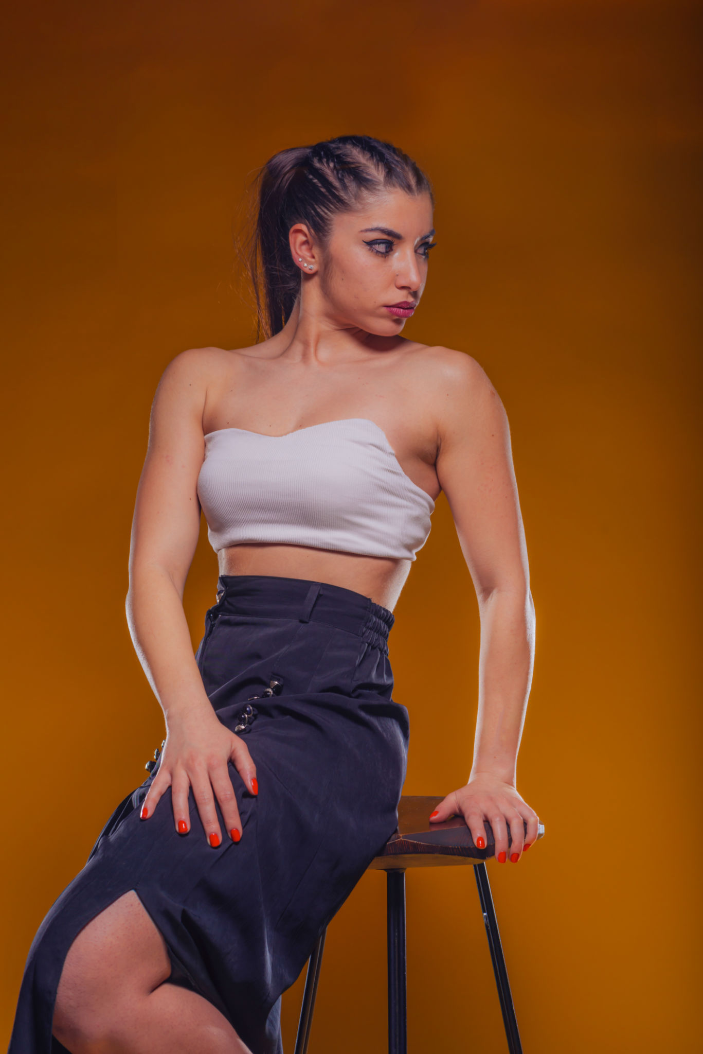 High fashion portrait of an attractive and stylish woman with dark hair and sexy neckline sitting on a high chair and posing inside a studio High fashion portrait of an attractive and stylish woman with dark hair and sexy neckline sitting on a high chair and posing inside a studio