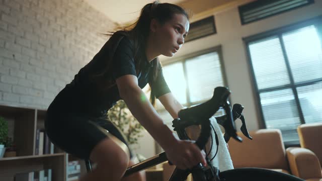 Asian woman cyclist. She is exercising in the house.By cycling on the trainer and play online bike games