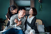 Playful young Asian family having fun playing at home while mother and daughter tickling father in bed. Family life with love and happiness