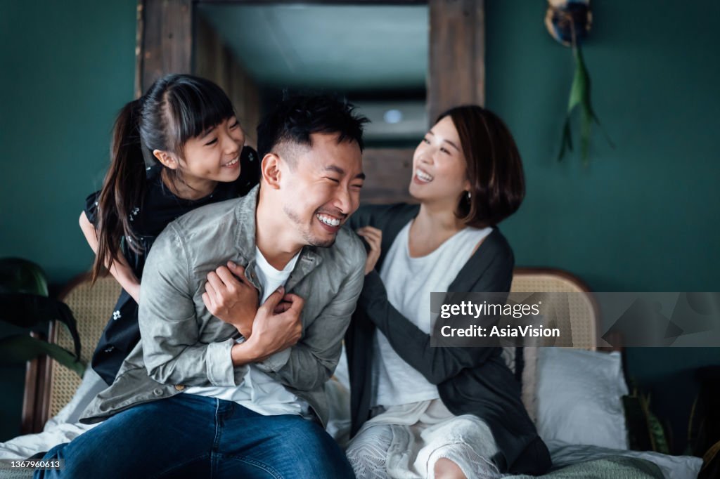 Playful young Asian family having fun playing at home while mother and daughter tickling father in bed. Family life with love and happiness