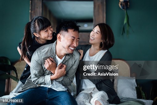 Playful young Asian family having fun playing at home while mother and daughter tickling father in bed. Family life with love and happiness Playful young Asian family having fun playing at home while mother and daughter tickling father in bed. Family life with love and happiness