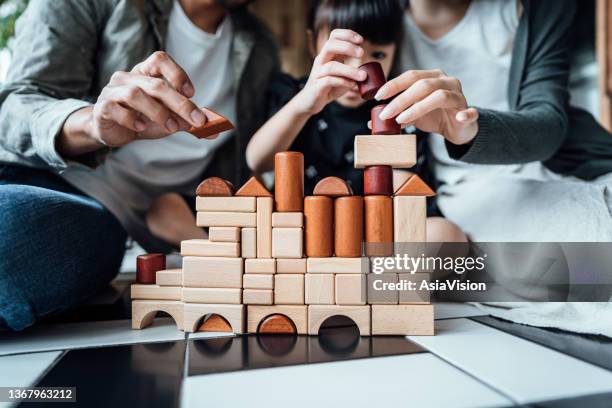 nahaufnahme der fröhlichen jungen asiatischen familie, die auf dem boden im wohnzimmer sitzt und spaß daran hat, holzbausteine mit der gemeinsamen tochter zu hause zu spielen - game house stock-fotos und bilder