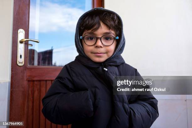 ritratto di ragazzo con gli occhiali che guarda la macchina fotografica con le mani in tasca di cappotto - solo bambini maschi foto e immagini stock