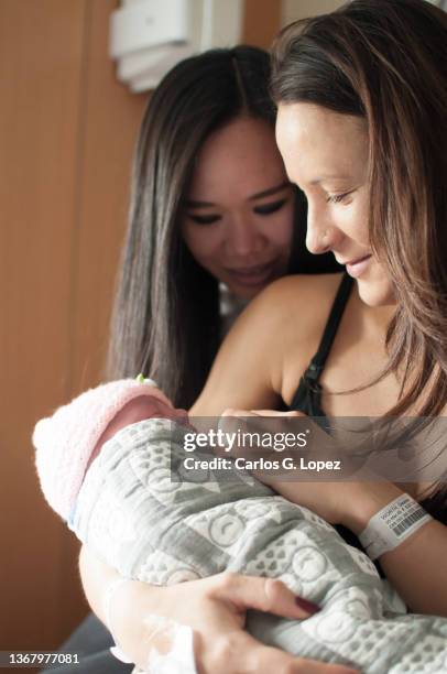 a mother holds her newborn baby daughter wearing a pink woolly hat and wrapped up in a blanket and smiles as her asian friend looks at the baby and smiles in a flat in edinburgh, scotland, uk - girls in bras photos stock pictures, royalty-free photos & images