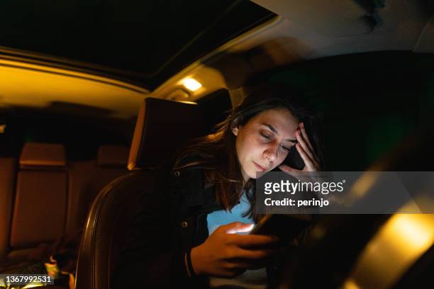 adolescente molesta, llorando en su coche, mientras usa el teléfono móvil - online bullying fotografías e imágenes de stock