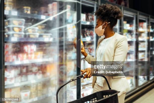 beautiful female with shopping cart opening supermarket freezer choosing what to buy. - frozen food bildbanksfoton och bilder