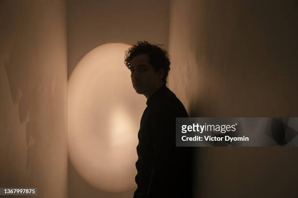 young curly man in the grey narrow room - claustrophobia stock pictures, royalty-free photos & images