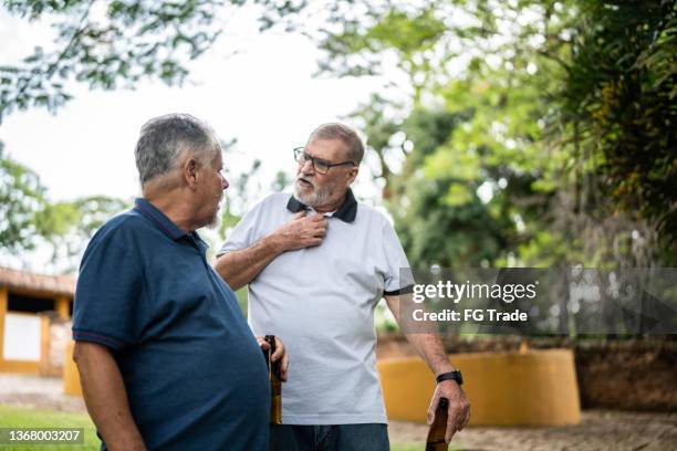 senior male friends having a conversation while walking in a park - friends fighting stock pictures, royalty-free photos & images