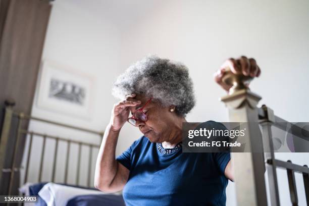 senior woman with headache sitting in the bed at home - verward stockfoto's en -beelden