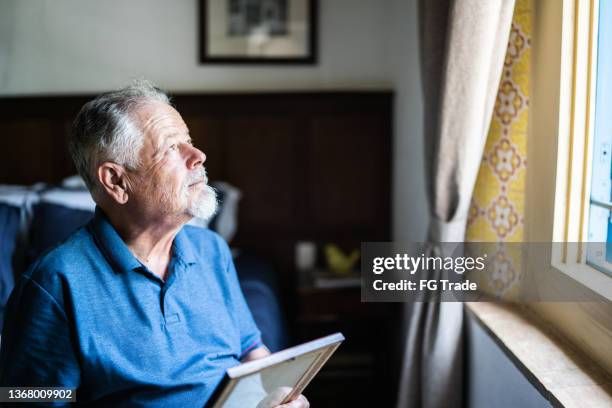 senior man holding a picture frame missing someone at home - love & death stock pictures, royalty-free photos & images