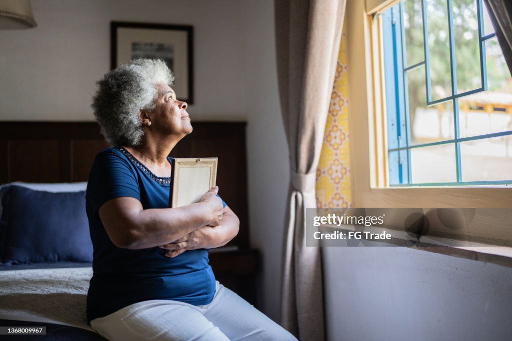 Mujer mayor sosteniendo un marco de fotos que extraña a alguien en casa