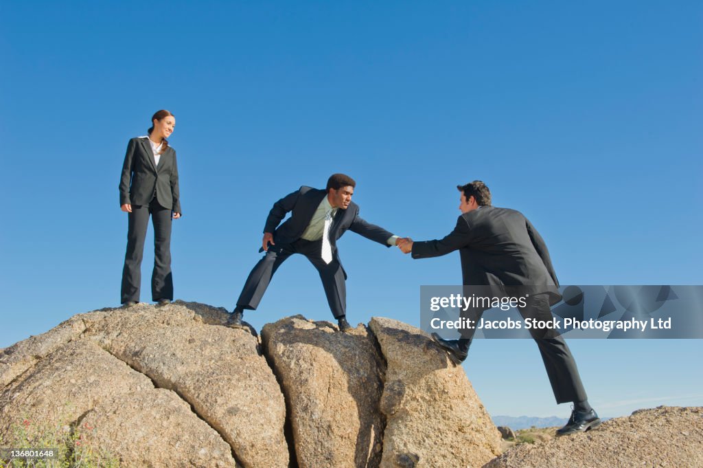 Businessman helping co-worker onto rock