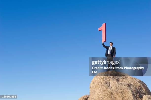 caucasian businessman on rock lifting large number 1 - prima esperienza foto e immagini stock