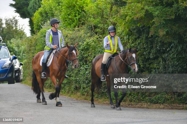 young couple ride their horses along road wearing safety gear and being seen by other road users , a queue of cars are waiting behind needing to pass when it is safe to do so. - horseback riding stock pictures, royalty-free photos & images