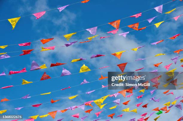 colorful papel picado-style bunting blowing in the wind against a sunny sky with light cloud - guirlande-de-fanions photos et images de collection