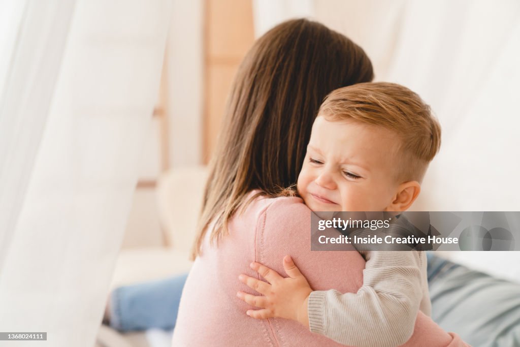 Caucasian mother lulling cradling her crying little small son daughter toddler infant newborn baby. Colics, teething health problems. Postnatal depression. Motherhood and childcare