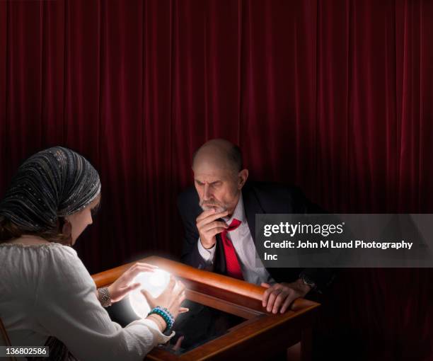 businessman visiting fortune teller with crystal ball - fortune teller table stock pictures, royalty-free photos & images