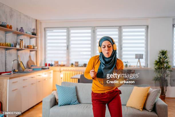 young muslim woman singing and dancing at home - women with hijab stock pictures, royalty-free photos & images