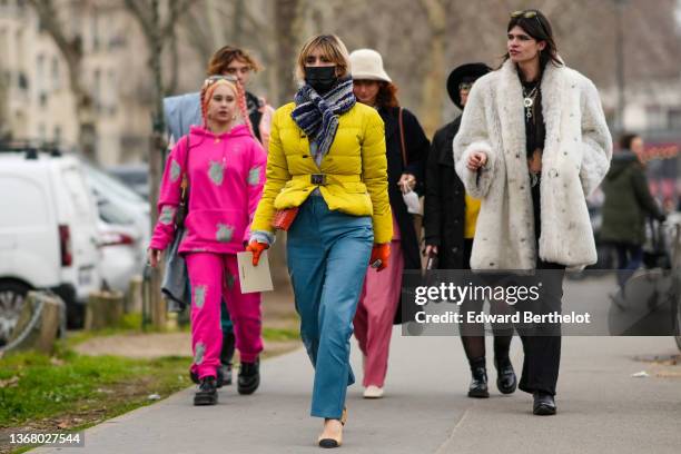 Guest wears a navy blue and white striped fluffy scarf, a yellow belted puffer jacket from Prada, a red leather nailed / studded bag from Paco...