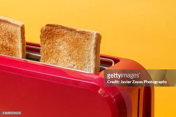 red toaster toasting two bread slices on yellow background - toaster fotografías e imágenes de stock