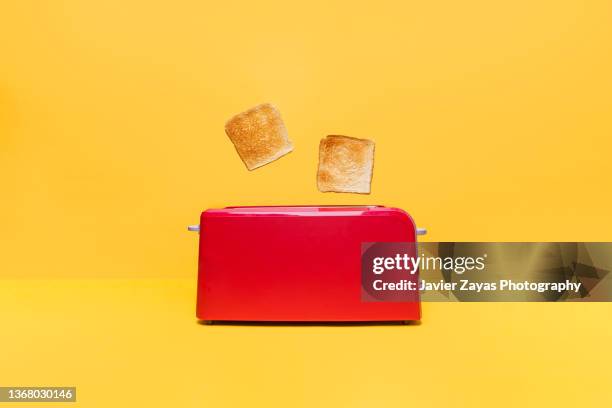 red toaster toasting two bread slices on yellow background - tostadora fotografías e imágenes de stock