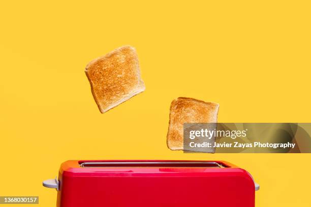 red toaster toasting two bread slices on yellow background - casa sezione foto e immagini stock