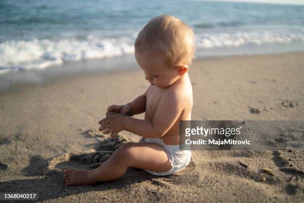 cute little baby boy sitting on the sand beach near by blue sea - beautiful beach babes 個照片及圖片檔