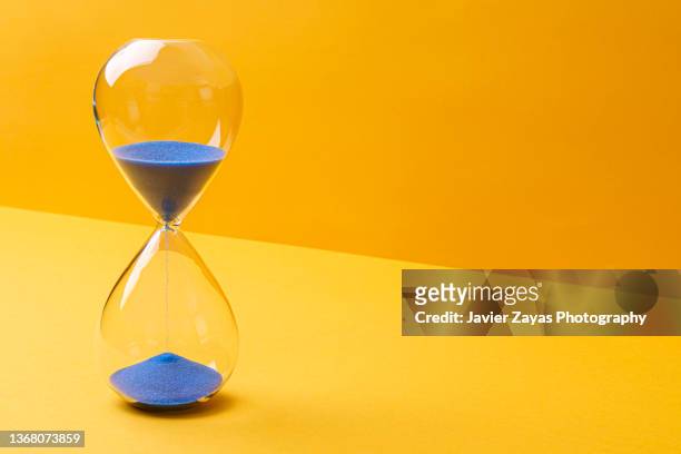 blue colored sand hourglass on yellow background - tijdslimiet stockfoto's en -beelden