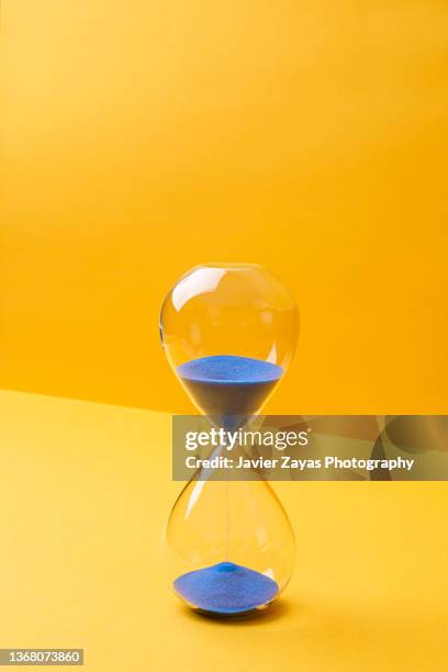 blue colored sand hourglass on yellow background - temps photos et images de collection