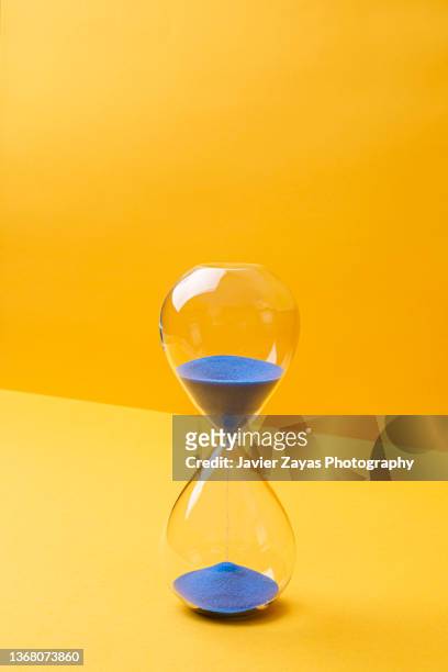 blue colored sand hourglass on yellow background - hourglass stock pictures, royalty-free photos & images