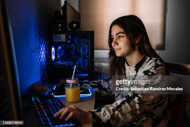 smiling young blonde sitting in front of her desktop computer - gaming imagens e fotografias de stock