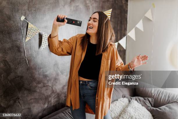 happy woman singing in the living room in front of the tv using the remote control - celebrating the songs voice of gregg allman backstage audience stockfoto's en -beelden