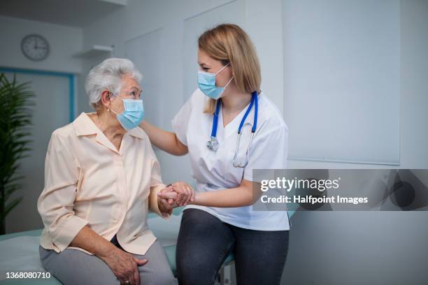 senior woman with female doctor wearing protective face masks and talking warmly in doctor's office. - doctor mask stock-fotos und bilder