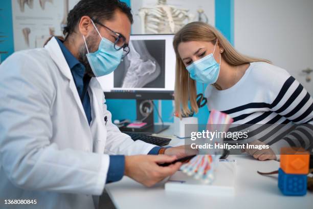 orthopedic doctor showing artificial skeleton of foot to young woman in clinic. - orthopedic surgeon ストックフォトと画像