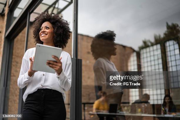 donna d'affari che distoglie lo sguardo e utilizza la tavoletta digitale in un ufficio - business vision foto e immagini stock