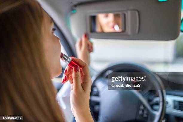 junge elegante frau, die in den autospiegel schaut, während sie lippenstift aufträgt - woman lipstick rearview stock-fotos und bilder