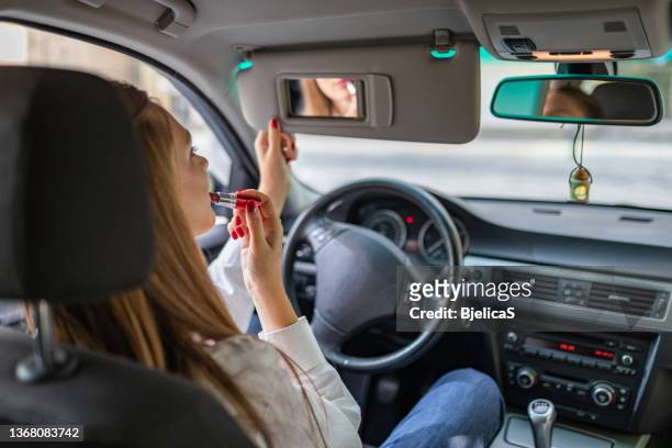 young elegant woman looking in the car view mirror while applying lipstick - woman lipstick rearview stock pictures, royalty-free photos & images