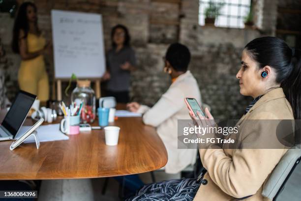 visually impaired businesswoman using smartphone and earphones during business meeting - accessibility blind stock pictures, royalty-free photos & images