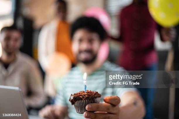 homem mostrando cupcake com vela de aniversário no trabalho - happy birthday - fotografias e filmes do acervo